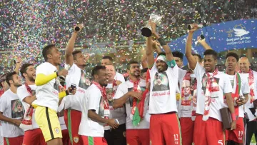 L'image montre une équipe de football célébrant une victoire. Les joueurs, vêtus de maillots assortis avec des t-shirts, levant un trophée en l'air, entourés de confettis multicolores. Ils semblent joyeux et enthousiastes, exprimant leur bonheur après avoir remporté un titre, probablement lors d'un tournoi ou d'une compétition. Les supporters en arrière-plan ajoutent à l'atmosphère festive.