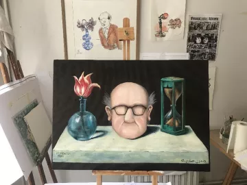 L'image montre une toile peinte, représentant un homme avec une tête large, des lunettes et des cheveux ébouriffés. Il est placé devant une table sur laquelle se trouvent un vase avec une fleur rouge, une sablier et un autre objet qui semble être une bouteille. En arrière-plan, on aperçoit des œuvres d'art accrochées au mur, ainsi qu'un chevalet. L'ensemble a une atmosphère artistique et quelque peu surréaliste.