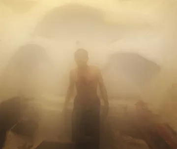 L'image montre un homme dans un environnement humide et brumeux, probablement à l'intérieur d'un hammam ou d'un sauna. La vapeur crée une atmosphère indistincte et floue, rendant les contours des objets difficilement visibles. L'homme est torse nu et semble se tenir debout, enveloppé par la vapeur qui l'entoure, ajoutant une sensation de chaleur et de sérénité à la scène. Les murs sont d'apparence texturée, typiques des espaces de bien-être.