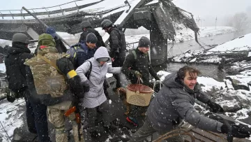 L'immagine mostra un gruppo di persone in un'area distrutta, probabilmente a causa di un conflitto o di un disastro. Alcune persone indossano abbigliamento militare, mentre altre sembrano civili. È in corso un salvataggio o un'evacuazione, con qualcuno che sta aiutando un'altra persona a attraversare il terreno difficile. La scena è caratterizzata da neve e condizioni atmosferiche difficili, suggerendo un ambiente critico e di emergenza. I volti mostrano preoccupazione e determinazione.