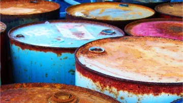 L'image montre plusieurs fûts en métal, probablement des fûts de pétrole ou d'huile. Ils sont empilés les uns à côté des autres, avec des couvercles rouillés et des étiquettes décolorées. La surface des fûts présente des signes d'oxydation, ce qui leur donne un aspect usé et ancien. Les couleurs variées du métal, allant du rouille au bleu clair, ajoutent à l'esthétique générale de la scène.