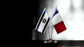 الصورة تظهر علمين صغيرين مرفوعين على قاعدة، أحدهما علم دولة إسرائيل ذو الألوان الزرقاء والبيضاء مع نجمة داود، والآخر هو علم دولة فرنسا بألوانها الثلاثة: الأزرق والأبيض والأحمر. الخلفية مظلمة، مما يبرز الأعلام بشكل واضح.