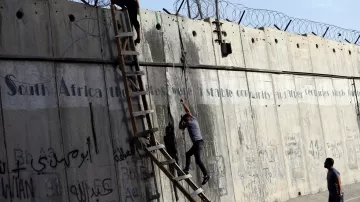 L'image montre une scène où deux personnes tentent de monter ou de descendre d'un mur de béton. Une échelle est appuyée contre le mur, et il y a des barbelés au sommet. Le mur présente également des graffitis ou des inscriptions, et l'environnement semble urbain. Les personnes semblent concentrées sur leur tâche, soulignant une dynamique d'effort et de défi.