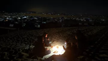در این تصویر، یک گروه از افراد در شب در حال دور هم نشستن در بیابان هستند. آنها در اطراف آتش نشسته‌اند و نور ملایم آتش نور را بر چهره‌هایشان می‌تاباند. در پس‌زمینه، می‌توان چادرها و نورهای دیگری را که در دوردست قرار دارند، مشاهده کرد. این صحنه حس صمیمیت و نزدیکی به طبیعت را منتقل می‌کند. همچنین، فعالیت‌های شبانه و سکوت بیابان به فضای تصویر عمق بیشتری می‌بخشد.