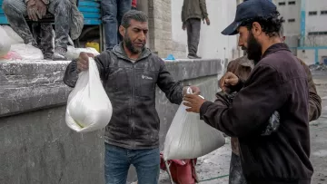L'immagine mostra un gruppo di uomini che stanno ricevendo o scambiando sacchetti. Gli uomini sembrano essere in un ambiente di lavoro, con segni di polvere sui loro vestiti, suggerendo che stiano partecipando a un'attività che richiede impegno fisico. I sacchetti possono contenere materiali o forniture, e l'atmosfera appare focalizzata e praticante. Sullo sfondo ci sono altri uomini e alcune strutture, che contribuiscono a un contesto di lavoro collettivo.