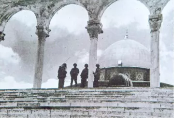 L'image montre une scène en noir et blanc, probablement historique, avec un groupe de soldats se tenant sur des marches devant un édifice. On peut apercevoir un dôme caractéristique au fond, ainsi que des arches en pierre en avant-plan. L'atmosphère est solennelle et le lieu semble chargé d'histoire. Les soldats sont habillés de manière militaire et semblent en position de garde.