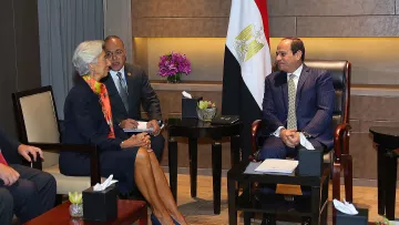 تظهر الصورة اجتماعًا رسميًا بين عدد من الشخصيات، حيث يجلس رجل يرتدي بدلة رسمية، على الأرجح هو رئيس دولة أو مسؤول حكومي، ويبدو أنه يناقش مع امرأة ترتدي ملابس أنيقة، ربما تكون مسؤولة دولية أو من منظمات كبيرة. يوجد شخص ثالث يقف بينهما، وهو يراقب الحوار. خلفهم، تُرى علم مصر، مما يشير إلى أن الاجتماع يتم في مصر أو يتعلق بشؤونها. الأجواء تبدو رسمية وودية.
