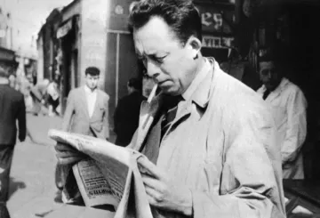 L'immagine ritrae un uomo in primo piano che legge un giornale, con una sigaretta tra le labbra. Indossa un soprabito chiaro e sembra assorto nella lettura. Sullo sfondo, si possono vedere altre persone che camminano per strada, in un contesto urbano. L'atmosfera è retro e richiama un'epoca passata, con un'illuminazione naturale e dettagli architettonici tipici di quel periodo.