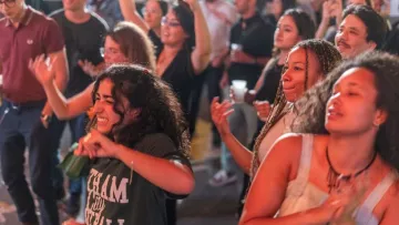 L'image montre un groupe de personnes en train de danser et de profiter d'une ambiance festive. On peut voir des personnes de différents âges, souriantes et s'amusant. Certaines gesticulent au rythme de la musique, tandis que d'autres sont concentrées sur le moment. L'éclairage est chaleureux, ce qui contribue à l'atmosphère joyeuse de l'événement.