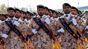 L'image montre un groupe de soldats en uniforme. Ils portent des uniformes camouflage et des képis distinctifs. Certains d'entre eux tiennent des fusils et affichent une attitude de discipline et de détermination. Des banderoles avec des inscriptions sont visibles sur leurs uniformes, et ils défilent en formation, visiblement lors d'une cérémonie ou d'un événement militaire. Le fond semble naturel, peut-être un terrain en extérieur.