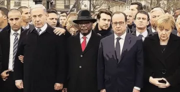 L'image montre un groupe de personnes en émoi, rassemblées dans un cadre public, probablement lors d'un événement solennel. On peut y voir des figures politiques en costumes, dont certaines portent des démarches sérieuses et concentrées. L'ambiance semble être empreinte de gravité et de solidarité. Les participants sont alignés et se regardent, ce qui indique une atmosphère de recueillement ou de soutien mutuel.