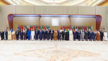 تظهر الصورة مجموعة من القادة ووزراء الخارجية المجتمعين في حدث رسمي. يقفون في صفوف مرتبة أمام خلفية مزينة بالعلم العربي، حيث تتواجد أعلام دول متعددة تشير إلى حدوث اجتماع أو قمة عربية. القادة يرتدون أزياء رسمية، بما في ذلك البذلات والعباءات، ويبدو عليهم الجدية والاهتمام بالمناسبة. الأجواء تعكس الطابع الرسمي والتاريخي لهذا اللقاء.