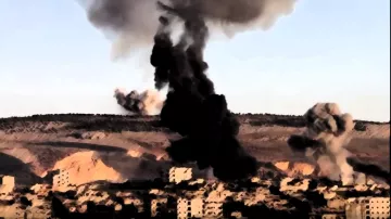 در این تصویر، دود سیاه و غلیظی از یک انفجار بزرگ در پس‌زمینه بلند می‌شود. در جلوی تصویر، ساختمان‌های آسیب دیده و ویران دیده می‌شوند که نشان‌دهنده آثار جنگ و تخریب هستند. در آسمان، عناصر متنوعی از انفجارها و آثار ناشی از آن به چشم می‌خورد، که حس خشونت و بحران را منتقل می‌کند. مناظر کوهستانی در دوردست نیز قابل مشاهده است.
