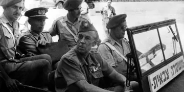 L'image montre un groupe de militaires assis dans un véhicule. Il y a plusieurs hommes en uniforme, portant des chapeaux distinctifs. Certains sont assis à l'avant, tandis que d'autres semblent être à l'arrière. L'atmosphère est solennelle, et il pourrait s'agir d'un moment lié à une opération ou une mission militaire. Le fond est flou, mais on aperçoit d'autres véhicules et un environnement urbain.