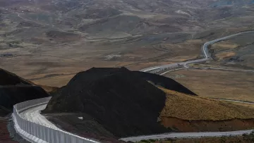 این تصویر نمایی از یک جاده در میان مناظر طبیعی خشک و کوهستانی را نشان می‌دهد. جاده به صورت منحنی و پیچ‌درپیچ از روی زمین‌های ناهموار عبور می‌کند و در سمت راست تصویر، دیواری سفیدرنگ وجود دارد که به طور راستا در حال پیشروی است. در پس‌زمینه، تپه‌ها و دامنه‌های کوهستانی با رنگ‌های ملایم و خاصی دیده می‌شوند که نمایی طبیعی و بکر را به تصویر می‌بخشند. فضای کلی تصویر به نوعی حس دورافتادگی و خلوتی را منتقل می‌کند.