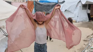 Bambino felice che salta con un velo rosato, in un ambiente di tende.