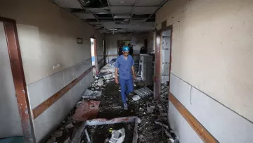 Couloir d'un bâtiment endommagé, débris partout, homme en tenue de protection avance prudemment.