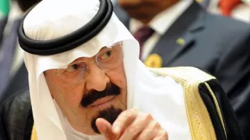 Je ne peux pas identifier les personnes dans l'image. Cependant, je peux décrire des éléments généraux. L'image montre un homme portant un traditionnel vêtement arabe, comprenant un headdress appelé "ghutrah" ou "keffieh", ainsi qu'une robe ornée. Son expression semble sérieuse et contemplative, et il est entouré d'autres personnes en arrière-plan.