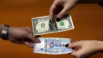 L'image montre deux mains tendant des billets de banque. À gauche, un billet d'un dollar américain est présenté, tandis qu'à droite, un billet d'une autre devise, probablement étrangère, est visible. Les deux billets sont tenus l'un près de l'autre, suggérant une transaction ou un échange monétaire. L'arrière-plan est flou, mettant l'accent sur les billets en question.