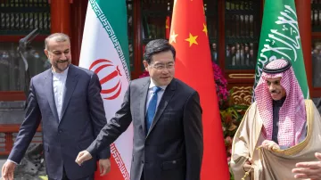 L'immagine mostra tre uomini che si trovano in un contesto formale e diplomatico, con bandiere dell'Iran, della Cina e dell'Arabia Saudita in background. I soggetti sembrano essere coinvolti in una discussione o in un incontro. L'atmosfera sembra prestigiosa e rappresenta un momento di incontro tra le nazioni.