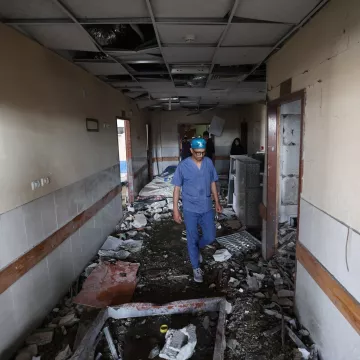 Couloir d'un bâtiment endommagé, débris partout, homme en tenue de protection avance prudemment.