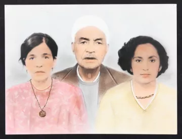 L'image représente un portrait de famille en couleur, où l'on voit trois personnes. Au centre se trouve un homme âgé avec une barbe grise, portant un chapeau blanc et un vêtement sobre. De chaque côté de lui, il y a deux femmes. À gauche, une femme avec des cheveux sombres, portant un haut rose et un collier. À droite, une autre femme avec des cheveux bouclés, habillée d'un haut jaune, qui affiche également un collier. L'arrière-plan est lumineux et flou, mettant en valeur les visages des sujets.