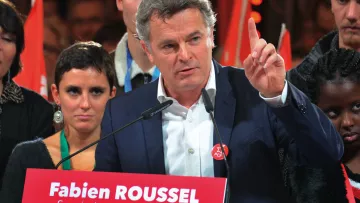 L'image montre un homme au premier plan, probablement en train de faire un discours. Il porte une veste et a l'air déterminé, levant un doigt comme s'il soulignait un point important. Derrière lui, plusieurs personnes l'écoutent, certaines regardant directement l'objectif. En bas de l'image, on peut voir une pancarte rouge avec le texte « Fabien ROUSSEL, Secrétaire national du PCF » et la date du 25 novembre 2018. L'ambiance semble être celle d'un congrès ou d'un rassemblement politique.