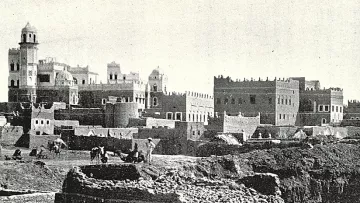 این تصویر نشان‌دهنده‌ی یک منطقه تاریخی است که در آن ساختمان‌های قدیمی با معماری سنتی دیده می‌شوند. در پس‌زمینه، چندین ساختمان با سقف‌های گنبدی و تزئینات خاص وجود دارد. همچنین افرادی در حال کار در زمین‌های جلویی دیده می‌شوند که ممکن است مشغول کشاورزی یا ساخت‌وساز باشند. این صحنه، حال و هوای زندگی روزمره و تاریخی را در یک جامعه قدیمی به تصویر می‌کشد.