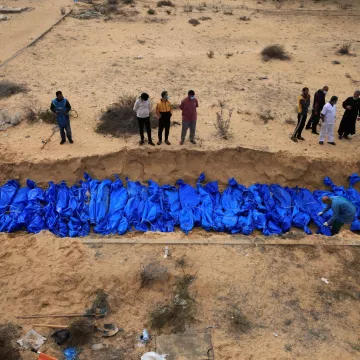 Des corps enveloppés de bleu sont placés dans une fosse, entourés de personnes en deuil.
