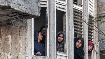 در این تصویر، تعدادی زن از پنجره‌های یک ساختمان قدیمی و دارای نمایی خراب نگاه می‌کنند. آن‌ها در حالت‌های مختلفی قرار دارند و به نظر می‌رسد نگران یا کنجکاو هستند. پوشش آنها شامل چادر و روسری است که نشان‌دهنده فرهنگ خاصی است. فضای تصویر به طور کلی تلخ و پر از تنش‌های اجتماعی به نظر می‌رسد.