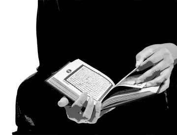 L'image montre une personne tenant un livre ouvert, probablement un texte sacré. Les mains sont bien visibles, feuilletant les pages, et l'arrière-plan est sombre, ce qui met en avant le livre. La combinaison entre les mains et le livre crée un contraste significatif, attirant l'attention sur l'acte de lire.