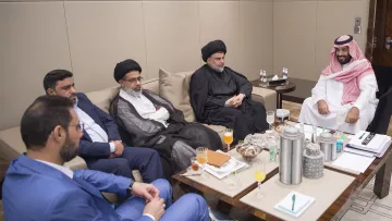 تظهر الصورة مجموعة من الأشخاص يجلسون في قاعة اجتماعات. يتواجد بعضهم بملابس تقليدية، بينما يرتدي آخرون ملابس رسمية. على الطاولة أمامهم توجد بعض المشروبات والوجبات الخفيفة. يبدو أن الاجتماع يتضمن مناقشات بين الأفراد، حيث يمتلك كل منهم تعبيرات جدية. المكان يبدو أنيقًا وعصريًا، مما يوحي بأهمية اللقاء.