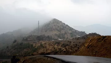 در این تصویر، یک جاده‌ا‌ی در کوهستان با شیب ملایم دیده می‌شود. در سمت راست، جاده به سمت دورتر ادامه پیدا می‌کند و در بالای تپه‌ها، ابرها در حال پایین آمدن و محو کردن قله‌ها هستند. روی تپه‌ها، درختان نسبتاً کوچک و فضاهای خشک دیده می‌شوند. در بالای تپه، یک دکل تلفن همراه نیز به چشم می‌خورد و چندین خودروی سفید رنگ در دور دست قابل مشاهده‌اند. جو تصویر ابری و مرطوب به نظر می‌رسد.