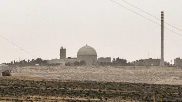تصویر نمایی از یک تاسیسات صنعتی یا علمی را نشان می‌دهد که دارای یک گنبد بزرگ و چند ساختمان دیگر است. در سمت راست تصویر، یک دودکش بلند به چشم می‌خورد که ممکن است مربوط به فعالیت‌های صنعتی باشد. فضای اطراف تصویر سرسبز نیست و بیشتر به بیابان یا زمین‌های خشک مشابهت دارد. آسمان نیز ابری و کدر به نظر می‌رسد. این تصویر ممکن است به یک مرکز تحقیقاتی یا نیروگاه اشاره داشته باشد.