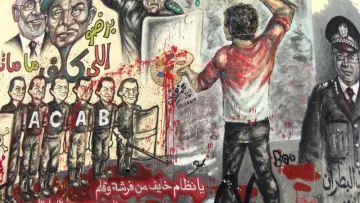 L'image montre un mural coloré, rempli de graffitis et d'illustrations. On y voit une scène dynamique où une personne, de dos, est en train de peindre avec un pinceau, probablement en train d'exprimer un message de frustration ou de résistance. Autour de cette figure, il y a diverses représentations de policiers et de figures autoritaires, certains avec des visages mécontents, indiquant une atmosphère de contestation. Le mur est éclaboussé de peinture rouge, ce qui pourrait symboliser la violence ou le sang, renforçant le message de lutte contre la répression. Les lettres "ACAB" sont visibles, ce qui fait référence à une phrase souvent associée à la critique des forces de police. L'ensemble de la composition semble porter un message fort sur l'opposition à l'autorité.
