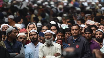 La imagen muestra una multitud de personas, muchas de las cuales llevan puestos kufis o tapones. La mayoría de las personas parecen estar prestando atención a algo en frente de ellos, algunos lucen serios y concentrados. Hay una gran diversidad de edades entre los asistentes y la atmósfera parece de expectativa. El fondo está lleno de más personas, lo que indica que es una reunión o evento masivo.