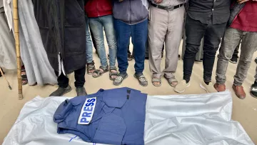 Des hommes entourent un gilet "PRESS" sur une bâche, en posture de recueillement.