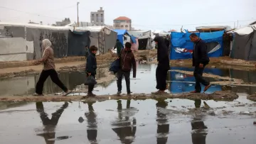 در تصویر، گروهی از مردم در یک منطقه نامناسب عبور می‌کنند. زیر پاهای آن‌ها آب جمع شده و انعکاس آن‌ها در آب دیده می‌شود. چادرهای موقتی در زمینه وجود دارند که به وضوح مشخص است. آسمان ابری و فضای کلی تصویر حاکی از شرایط سخت و نامساعد است. افراد در حال حرکت به سمت مقصدی مشخص هستند و لباس‌های آن‌ها نشان‌دهنده وضعیت اقتصادی و اجتماعی‌اشان است.