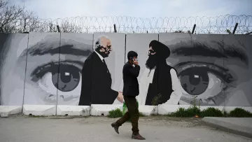 در این تصویر یک مرد در حال راه رفتن در کنار دیواری با یک نقاشی بزرگ است. دیوار دارای تصاویری از دو مرد است که به نظر می‌رسد در حال گفت‌وگو هستند. این نقاشی شامل چشمان بزرگی است که به وضوح بر روی دیوار کشیده شده و احساس عمیقی از توجه و نظارت را منتقل می‌کند. محیط اطراف خیابانی است و مرد به نظر می‌رسد مشغول صحبت کردن با تلفن همراهش باشد. طراحی و رنگ‌ها نسبتاً ملایم و معاصر به نظر می‌رسند.