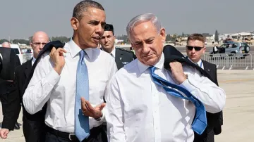 L'image montre deux hommes, habillés en costume, marchant ensemble sur un tarmac. L'un porte une cravate bleue et l'autre une cravate claire. Ils semblent engagés dans une conversation. En arrière-plan, on peut apercevoir des membres de la sécurité et des véhicules. Le ciel est clair, et l'environnement semble être un aéroport.