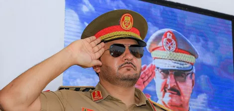 ضابط عسكري يرتدي زيًا رسميًا ونظارات شمسية، يؤدي تحية عسكرية.