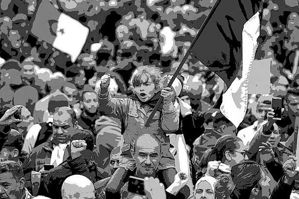 L'image montre une foule rassemblée lors d'une manifestation. Au premier plan, une petite fille se tient sur les épaules d'un adulte, brandissant un drapeau. Elle semble enthousiaste et déterminée, levant le poing. La foule autour d'elle est dense, avec des visages variés et des drapeaux visibles en arrière-plan. L'atmosphère est dynamique et engagée, évoquant un sentiment collectif et de solidarité.